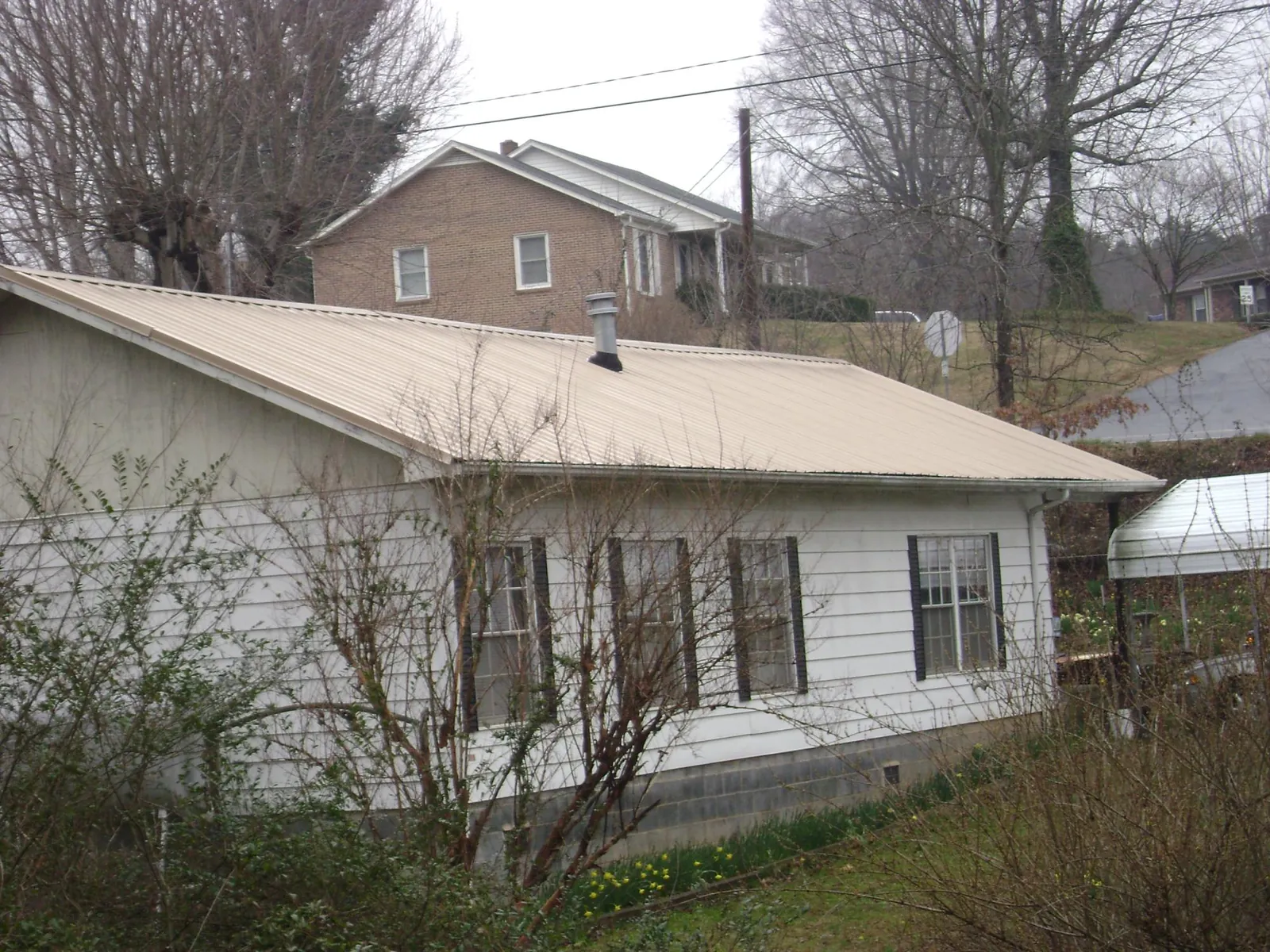 Tan metal roof on a white sided house set into a hillside — Commercial Roofing by Roofing Brothers in Winchester